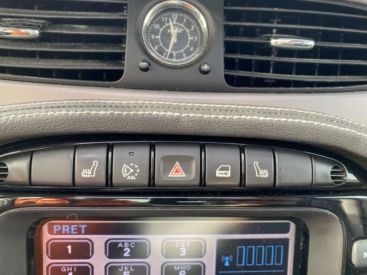 Gros plan sur la console centrale de la Jaguar XJ noire, montrant les boutons de sièges chauffants et l’horloge analogique.
