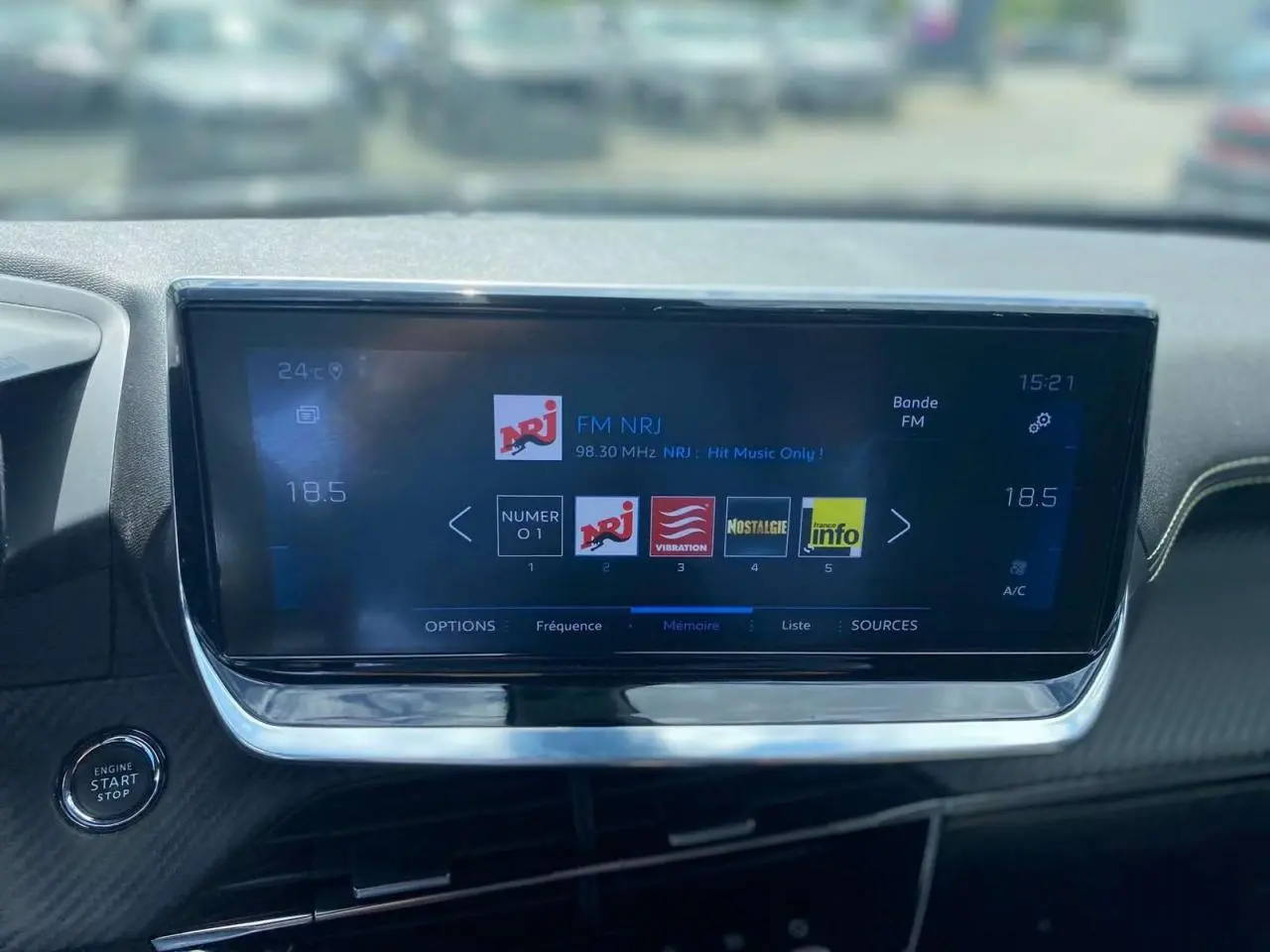 Vue rapprochée de l’écran tactile central de la Peugeot 2008 gris foncé, affichant la radio FM NRJ et le bouton start/stop.