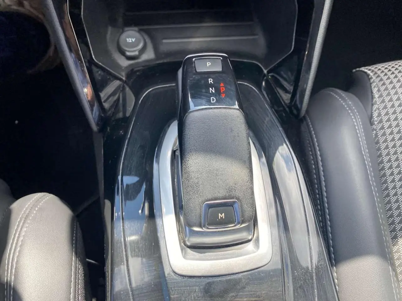 Gros plan sur la commande de boîte automatique noire au centre de la console d'une Peugeot 2008, avec siège gris à droite.