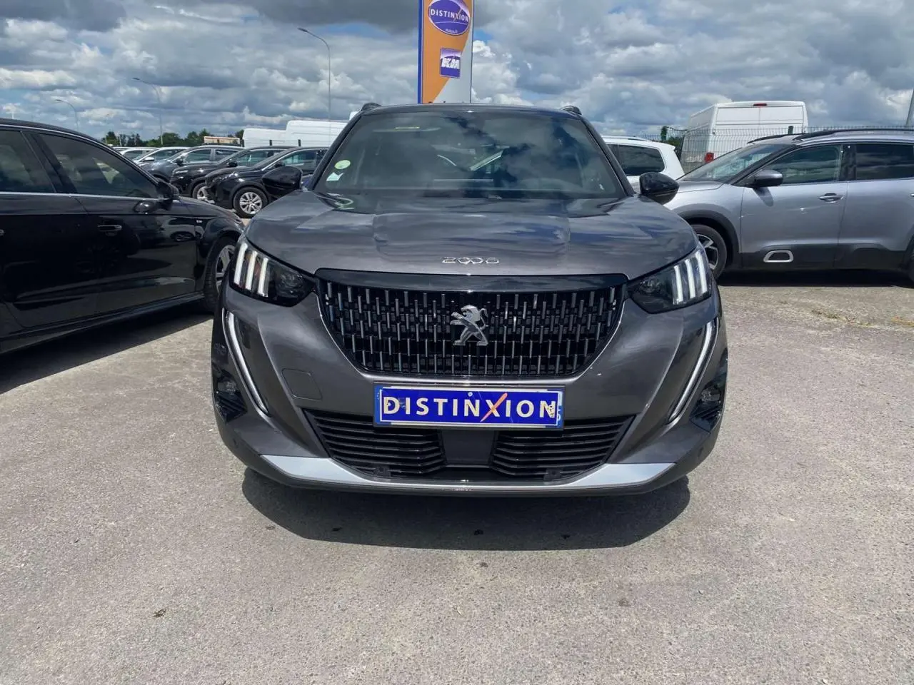 Vue avant du Peugeot 2008 gris foncé avec calandre noire et feux LED à signature 3 griffes, sur parking extérieur.