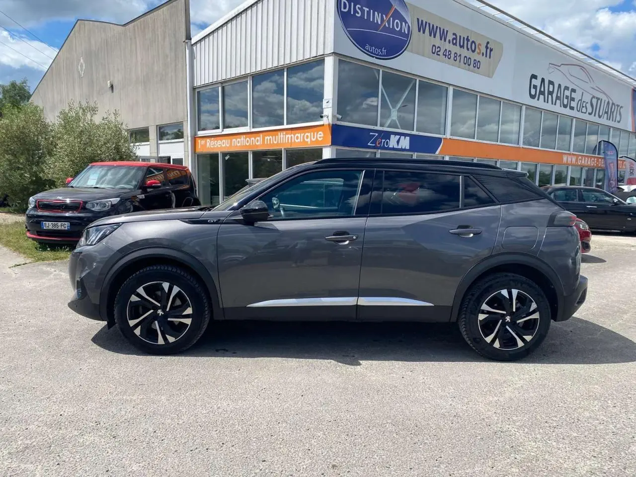 Profil droit d’un Peugeot 2008 GT gris foncé avec toit noir et jantes alliage 17'' bi-tons, stationné devant un garage.