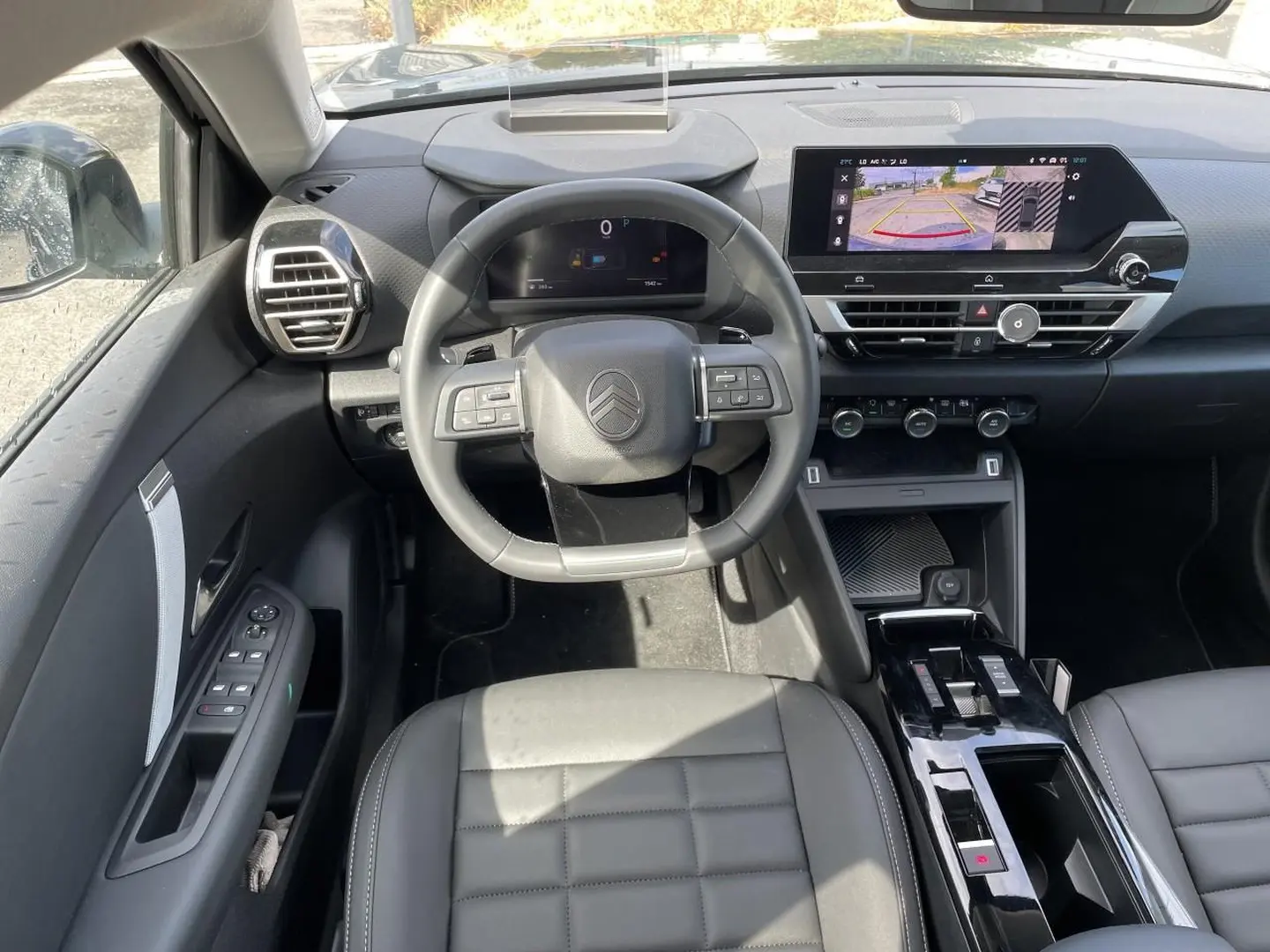 Vue intérieure avant centrée sur le volant cuir et tableau de bord avec écran tactile affichant la caméra de recul du Citroën C4 X noir.