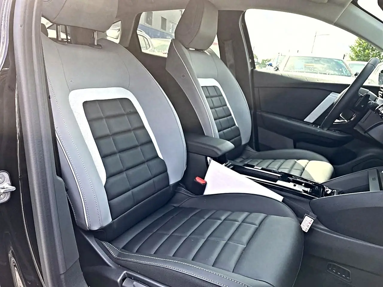 Vue intérieure côté conducteur de la Citroën C4 X noire 2025, sièges bi-matière gris et noir avec accoudoir central.