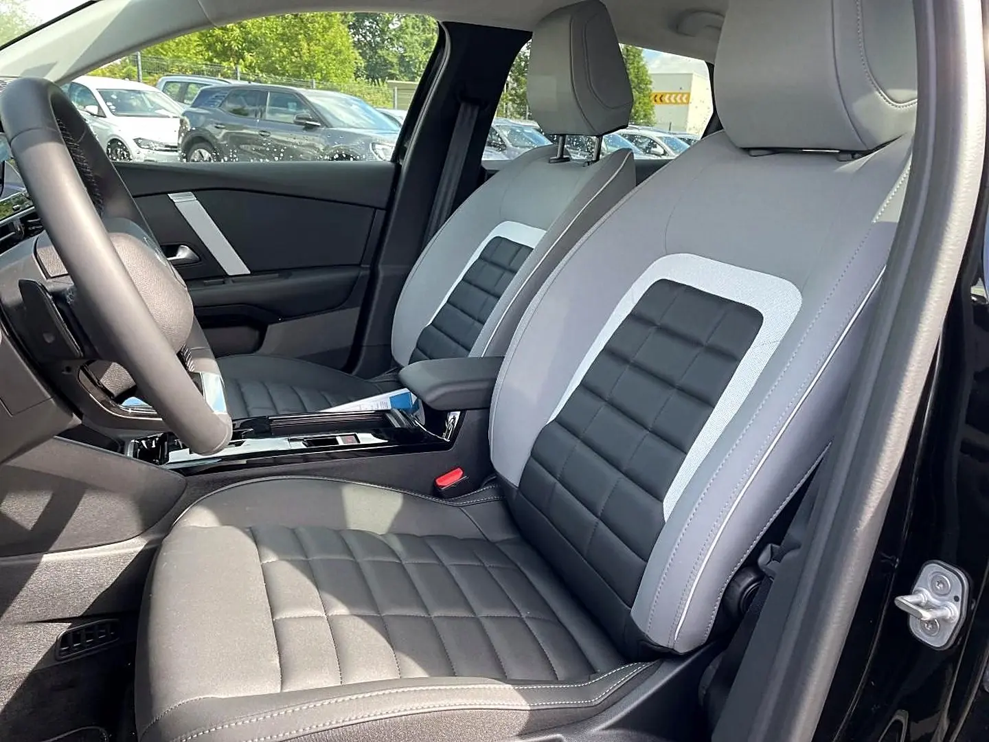 Vue intérieure côté conducteur de la Citroën C4 X noire 2025, sièges bi-tons gris et noir avec accoudoir central.