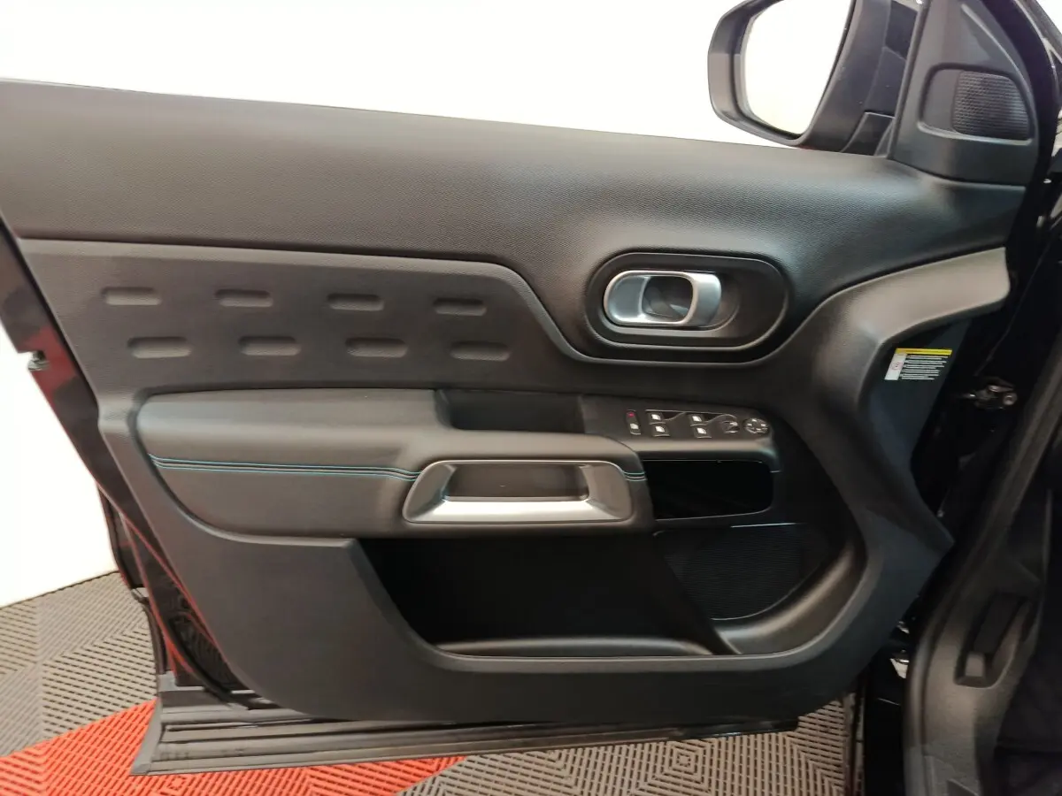 Vue intérieure côté gauche de la porte avant noire du Citroën C5 Aircross 2024 avec commandes de vitres et poignée argentée.