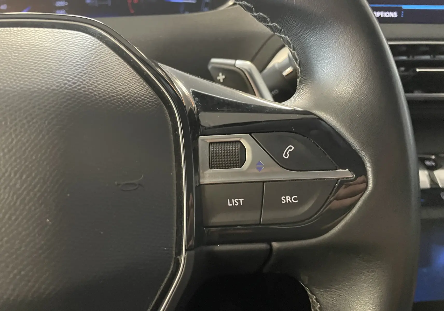 Gros plan sur les commandes à droite du volant noir du Peugeot 5008 blanc nacré, boutons list, src et appel téléphonique.