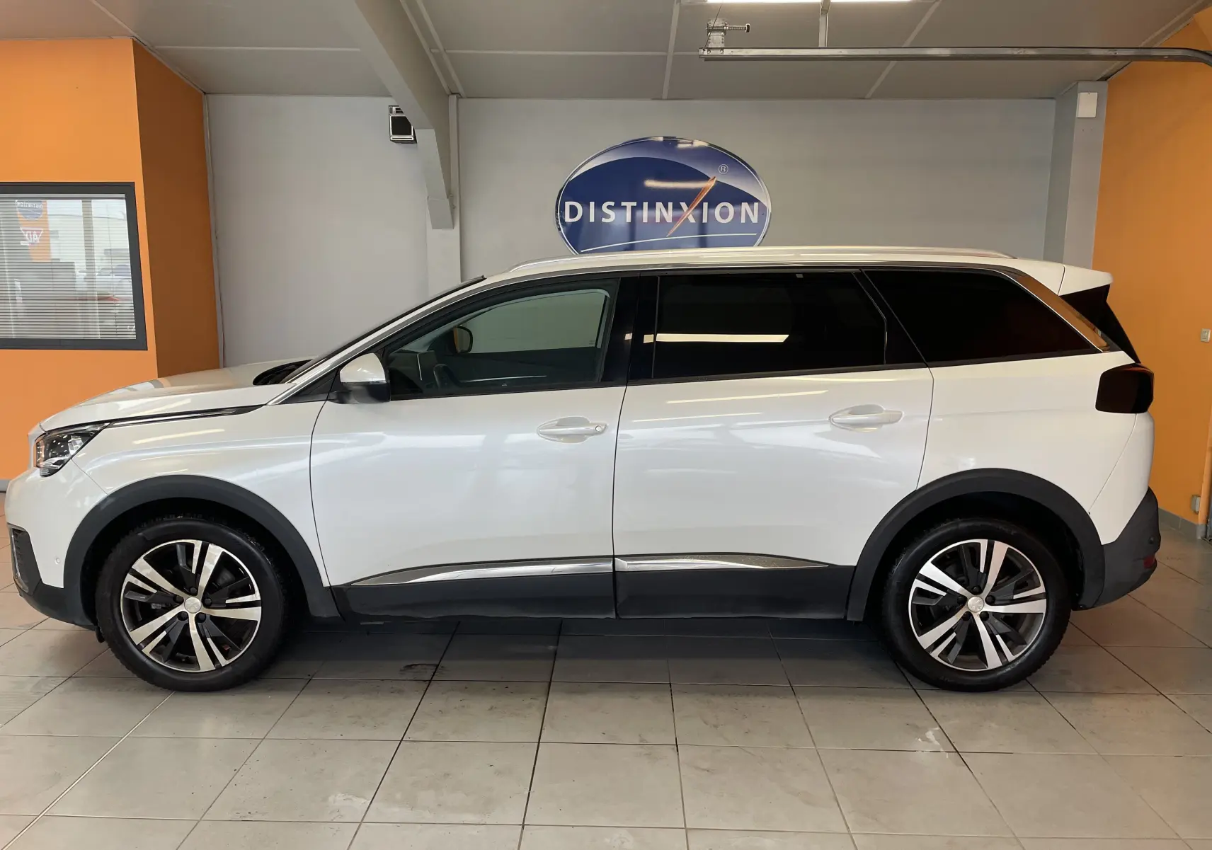 Peugeot 5008 blanc nacré vu de profil côté gauche, avec jantes alliage et vitres teintées dans un showroom.