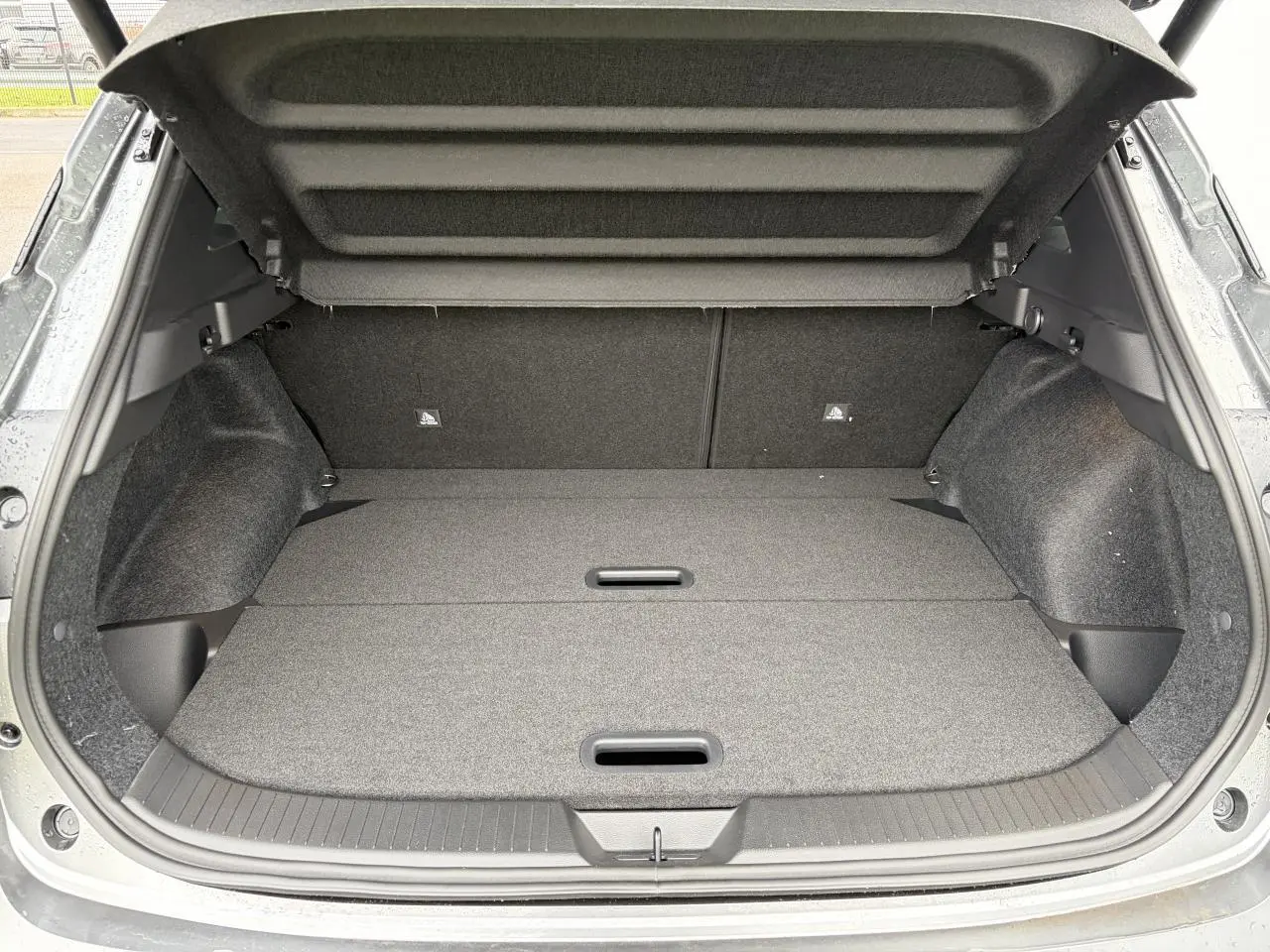 Coffre ouvert du Nissan Qashqai III 1.5 Hybrid e-Power gris foncé, montrant un espace de chargement plat et propre.