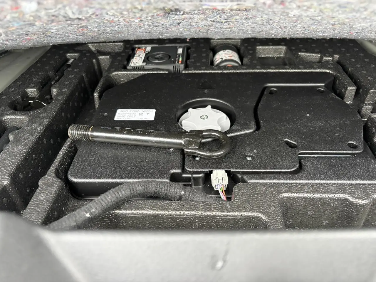 Gros plan sur le compartiment de rangement sous le plancher de coffre du Nissan Qashqai III, avec outil de remorquage visible.