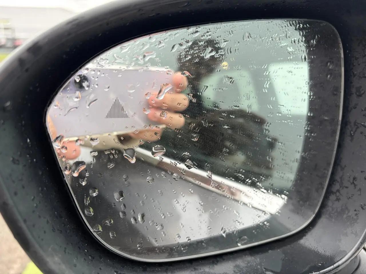 Rétroviseur extérieur droit du Nissan Qashqai 2025 gris foncé avec gouttes de pluie et témoin d'angle mort.