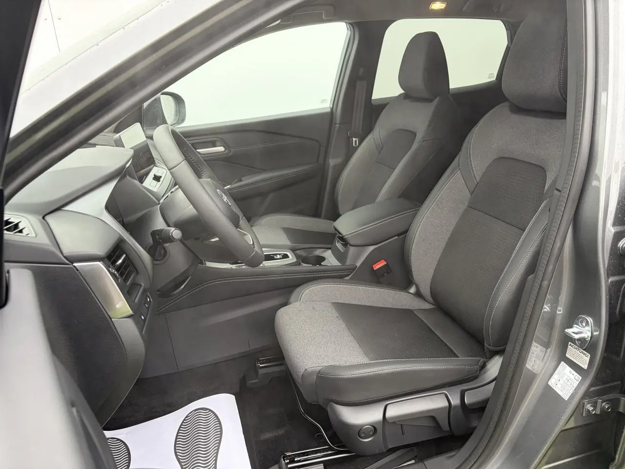 Vue intérieure côté conducteur du Nissan Qashqai 2025 gris foncé, sièges tissu et TEP noirs avec console centrale et volant cuir.