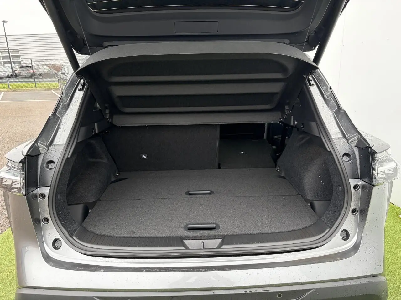 Coffre ouvert vu de l'arrière d'un Nissan Qashqai III gris foncé métallisé avec banquette arrière partiellement rabattue.
