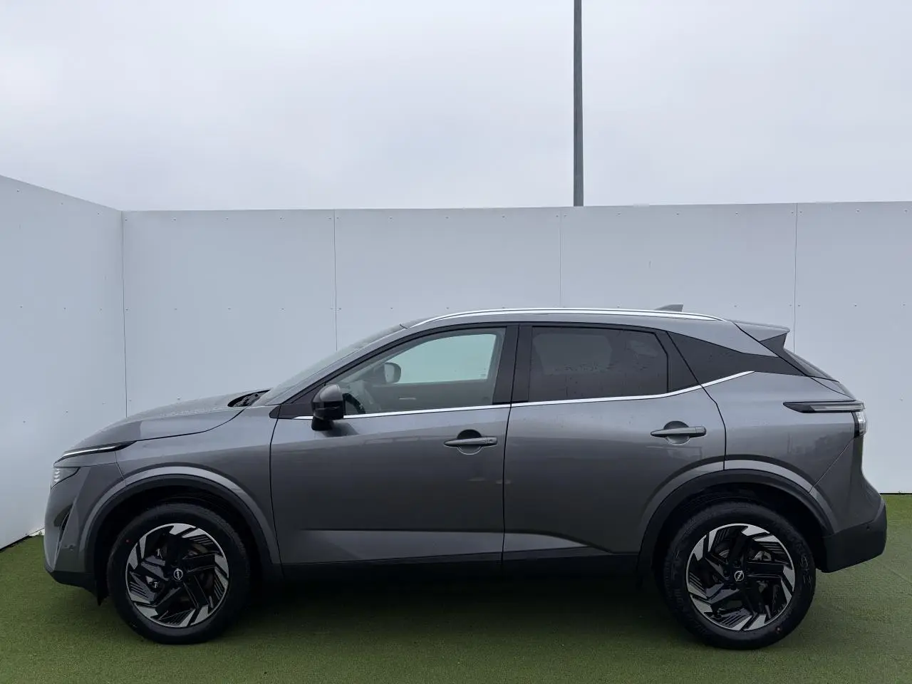 Profil droit du Nissan Qashqai III 1.5 Hybrid E-Power 2025 en gris métallisé avec jantes alliage noires et toit contrasté.