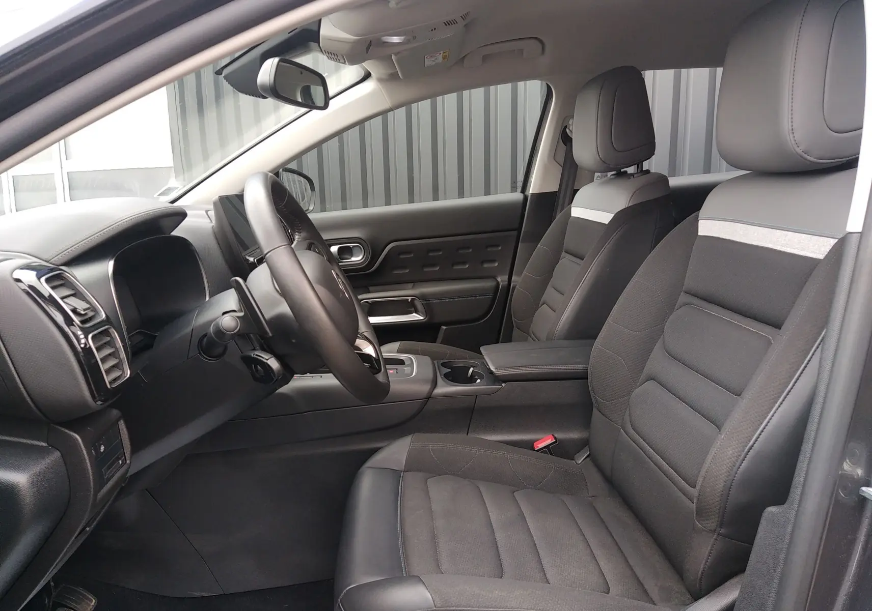 Vue intérieure côté conducteur du Citroën C5 Aircross 2023, sièges tissu noir avec détails gris et tableau de bord moderne.