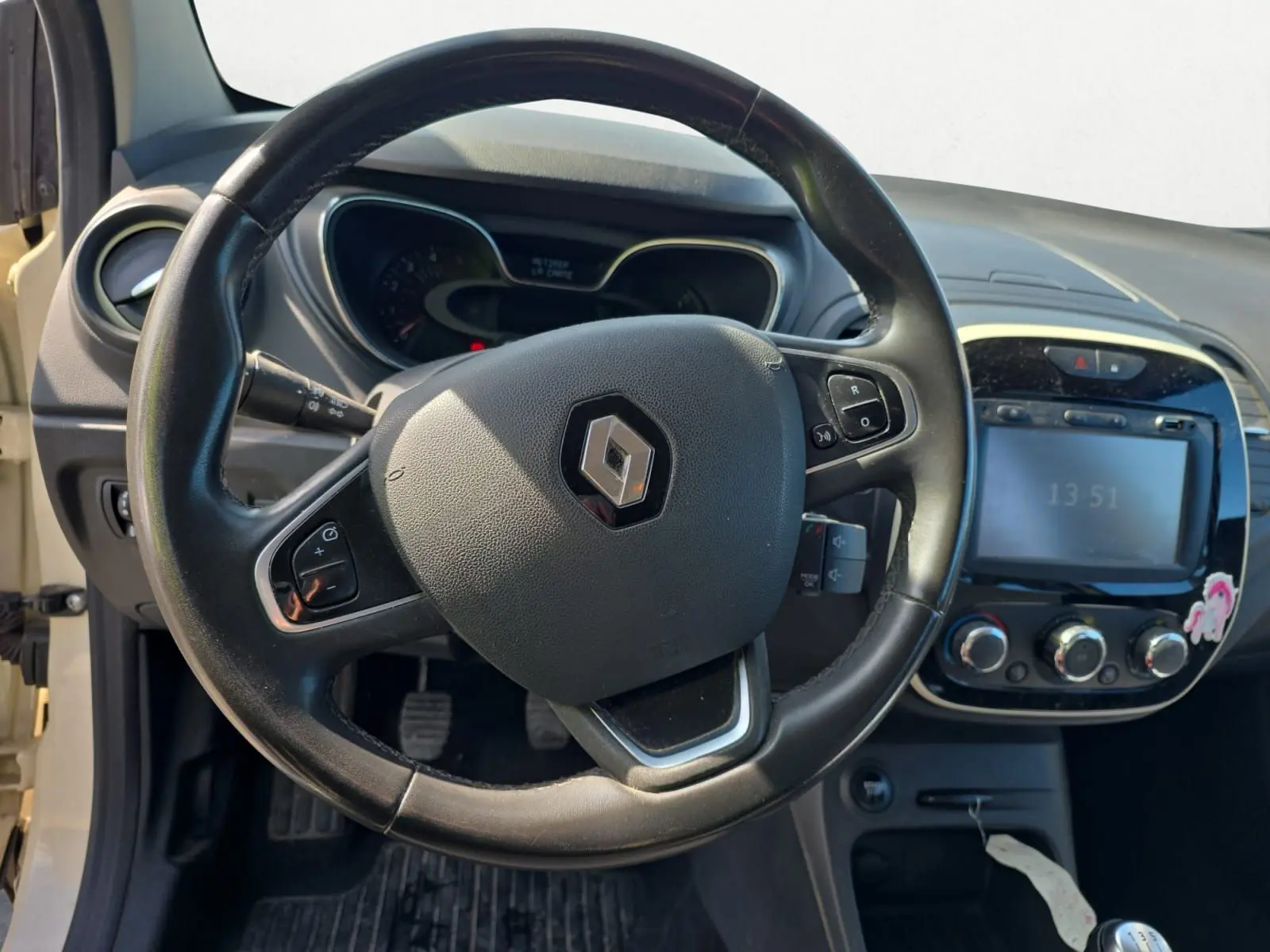 Vue rapprochée du tableau de bord du Renault Captur ivoire 2018, mettant en valeur l'écran GPS et les commandes de climatisation.