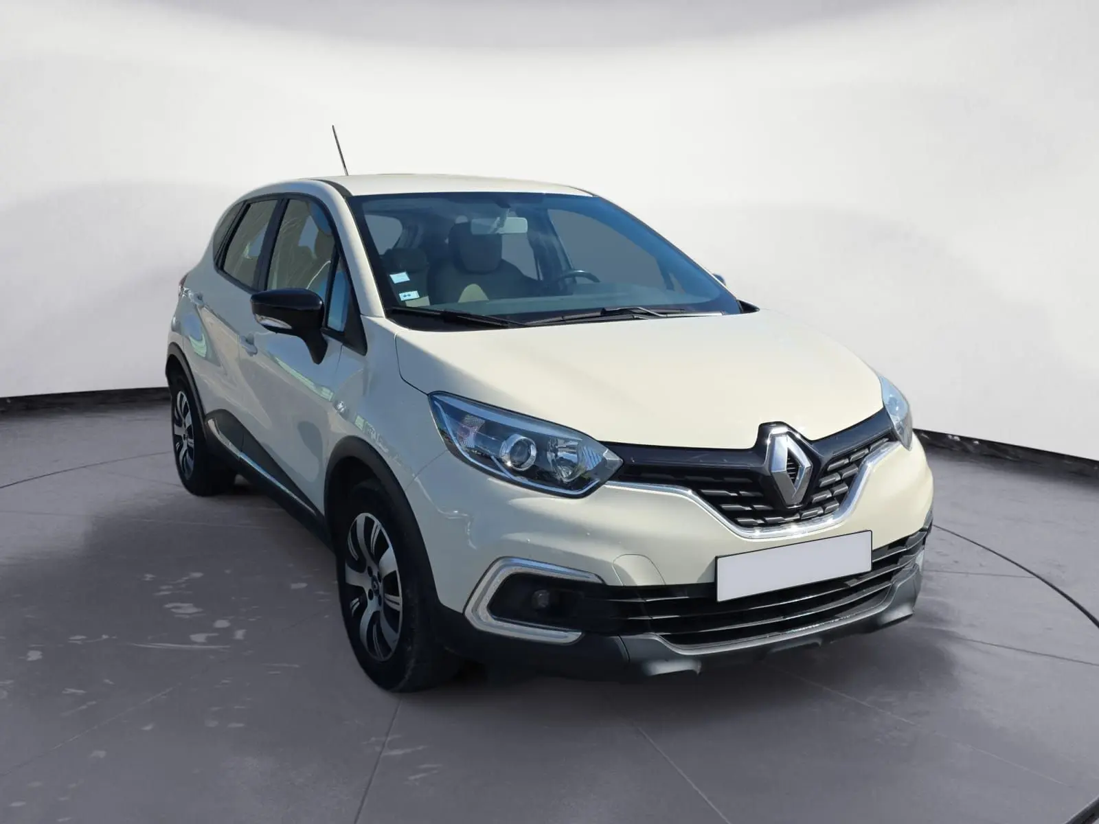 Profil droit d'un Renault Captur ivoire 2018 avec jantes alliage et protections noires sur un sol gravillonné.