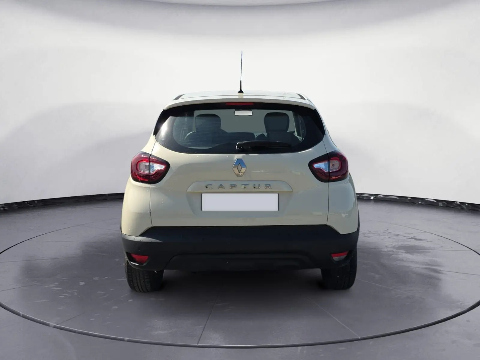 Vue 3/4 arrière droite d'un Renault Captur ivoire 2018 avec jantes alliage et protections noires sur un terrain extérieur.