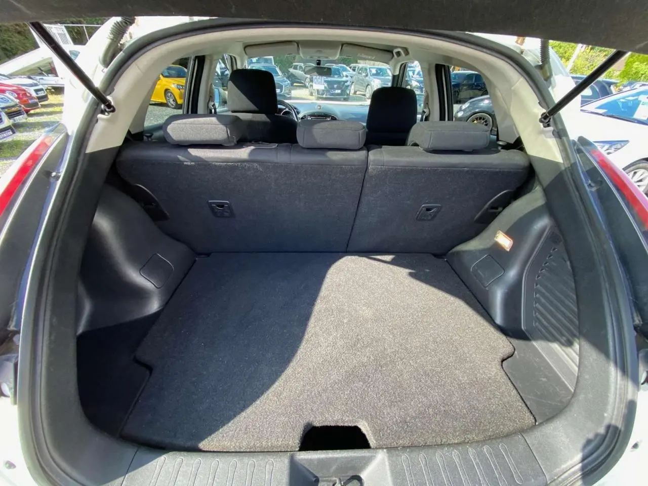 Coffre ouvert d’un Nissan Juke blanc, vue arrière montrant la banquette arrière et le plancher de coffre plat.