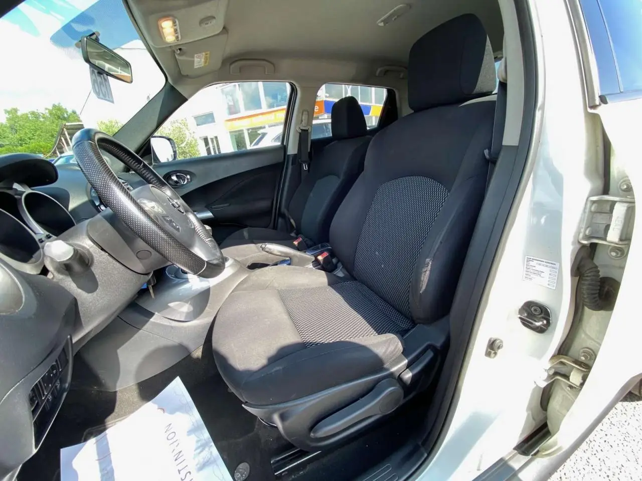 Vue intérieure côté conducteur du Nissan Juke blanc 2017, montrant les sièges avant en tissu noir et le volant multifonction.