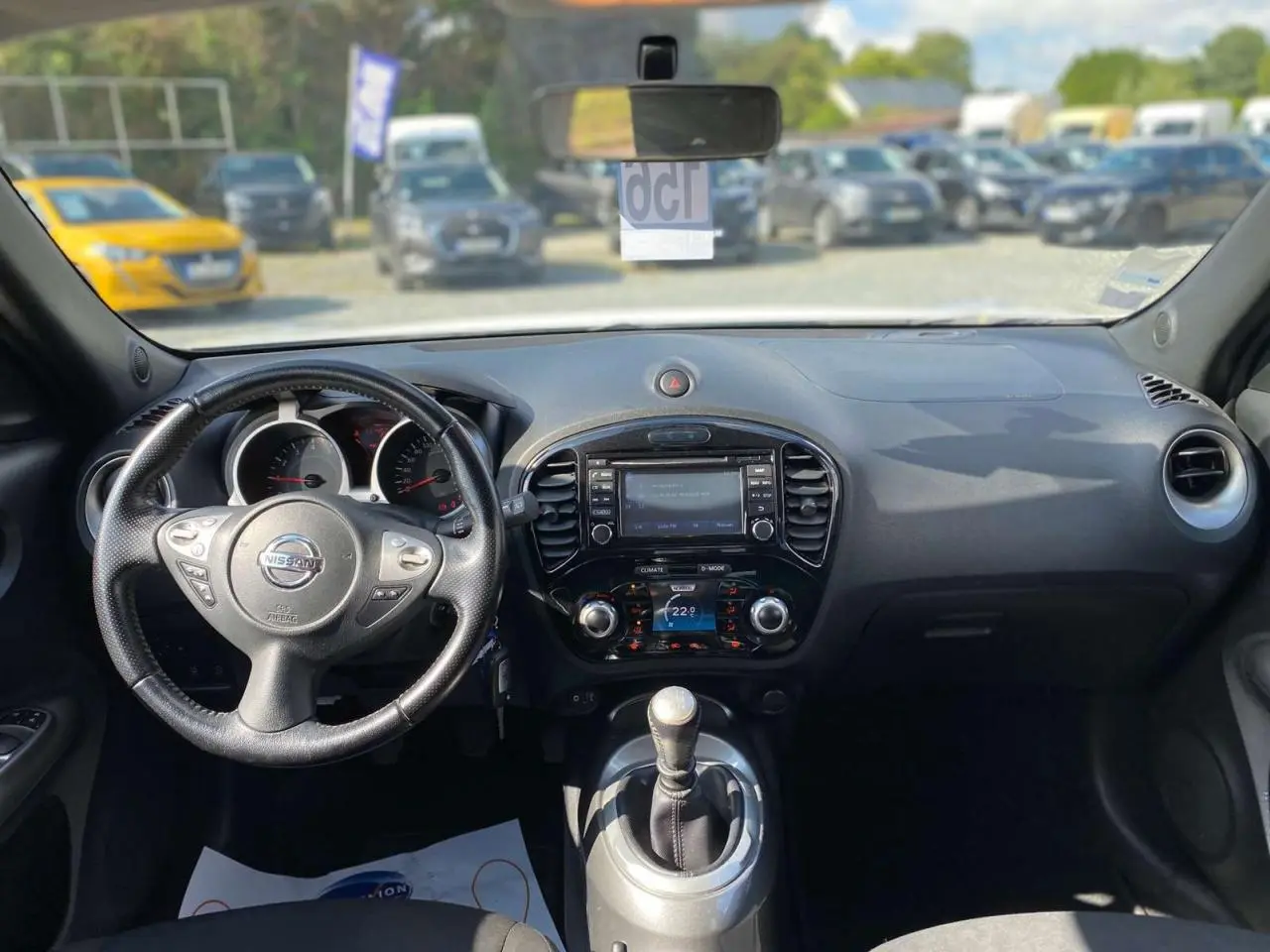 Vue intérieure du tableau de bord et volant d’un Nissan Juke blanc de 2017 avec boîte manuelle et écran central.
