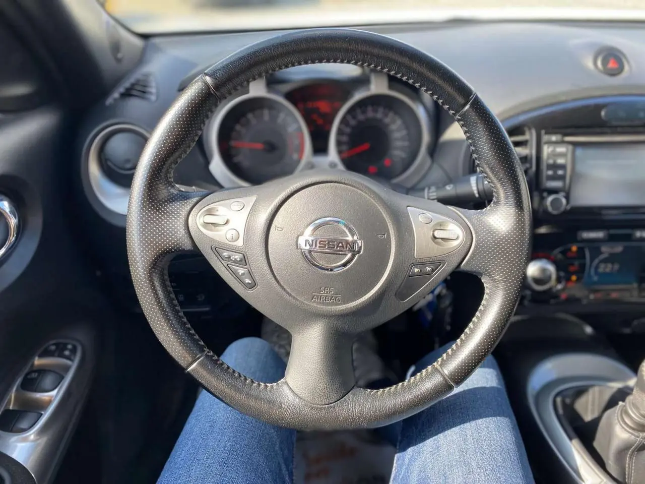 Vue intérieure centrée sur le volant noir perforé du Nissan Juke 2017 avec commandes intégrées et tableau de bord en arrière-plan.