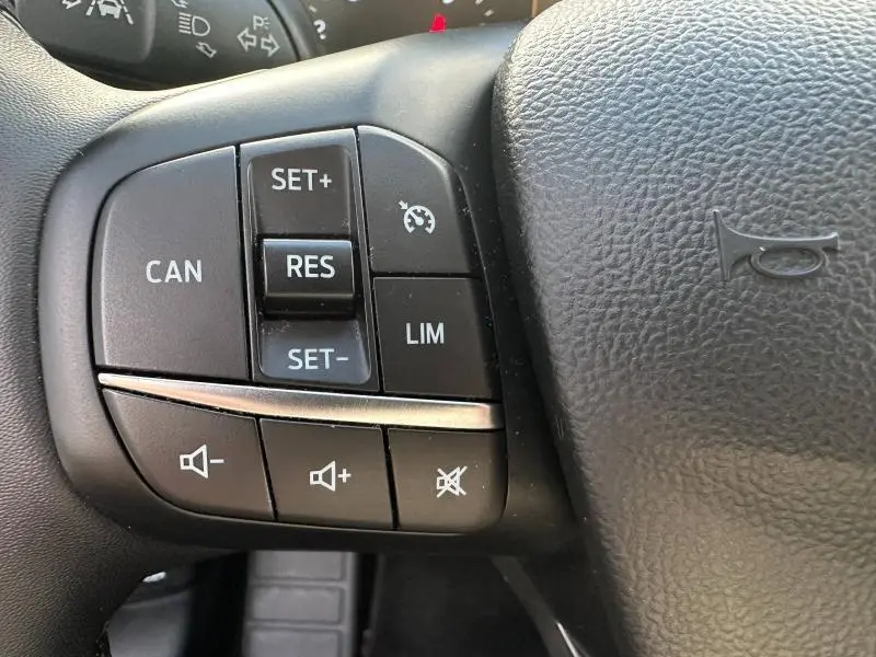 Gros plan sur les commandes du volant cuir noir de la Ford Focus 2023, boutons de régulateur de vitesse et volume sonore.