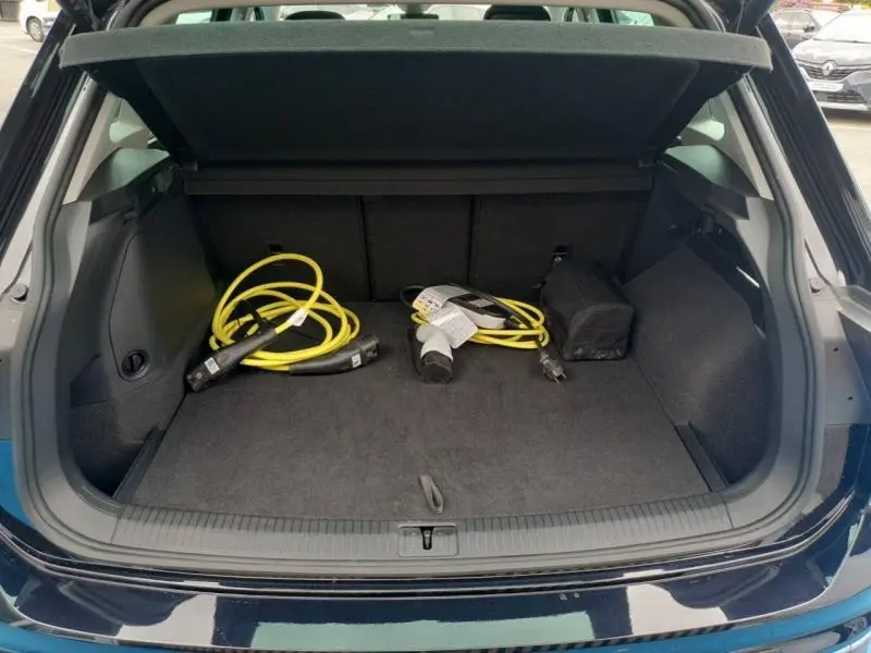 Coffre ouvert du Volkswagen Tiguan noir intense nacré, montrant câbles de recharge jaune et intérieur spacieux.