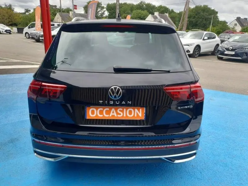Vue arrière d’un Volkswagen Tiguan 1.4 eHybrid noir intense nacré avec badge hybride et plaque "OCCASION" orange.