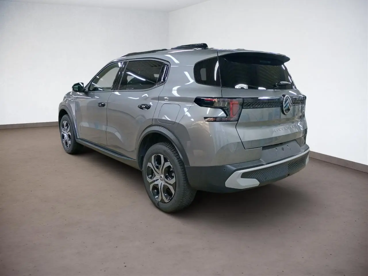 Vue 3/4 arrière droite du Citroën C3 Aircross gris Mercury avec vitres surteintées et barres de toit noires.