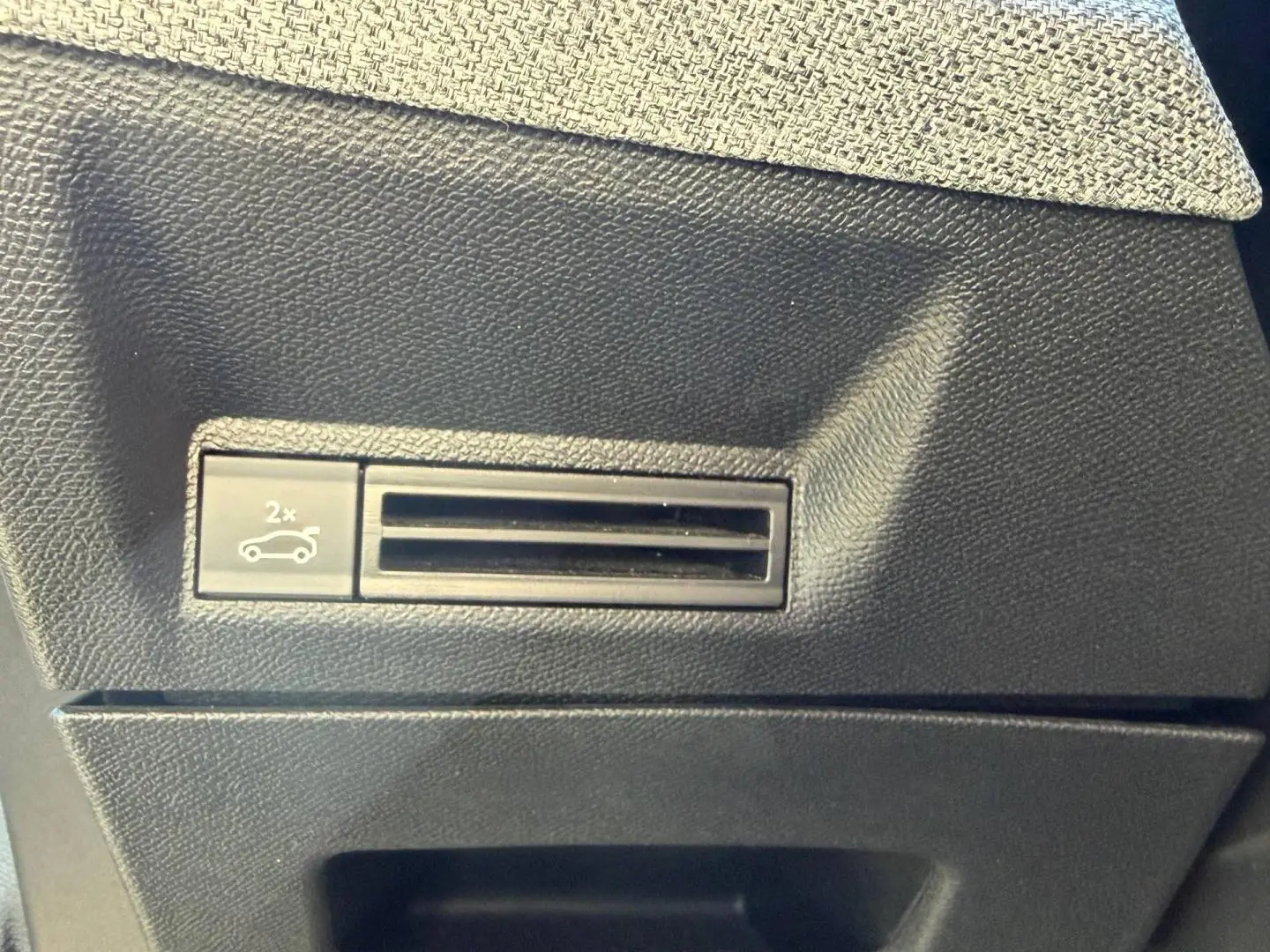 Détail du bouton d'ouverture électrique du coffre sur la console intérieure noire du Peugeot 5008 Hybrid blanc.
