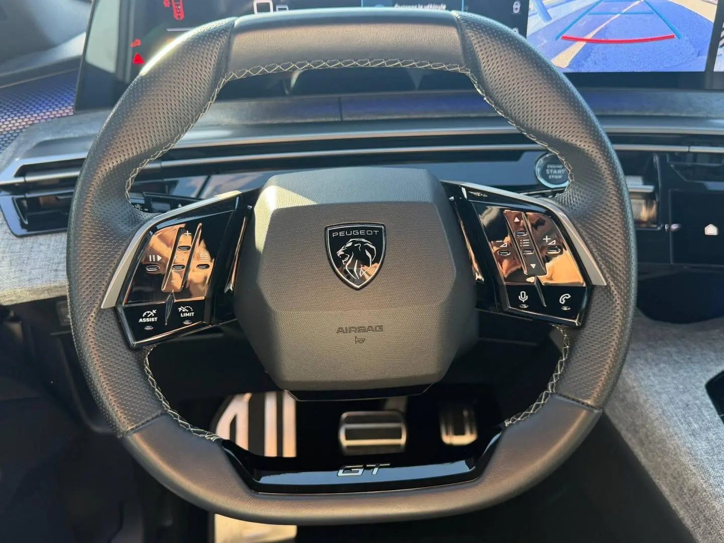 Vue rapprochée du volant cuir multifonction noir avec logo Peugeot et inscription GT, tableau de bord gris clair en arrière-plan.
