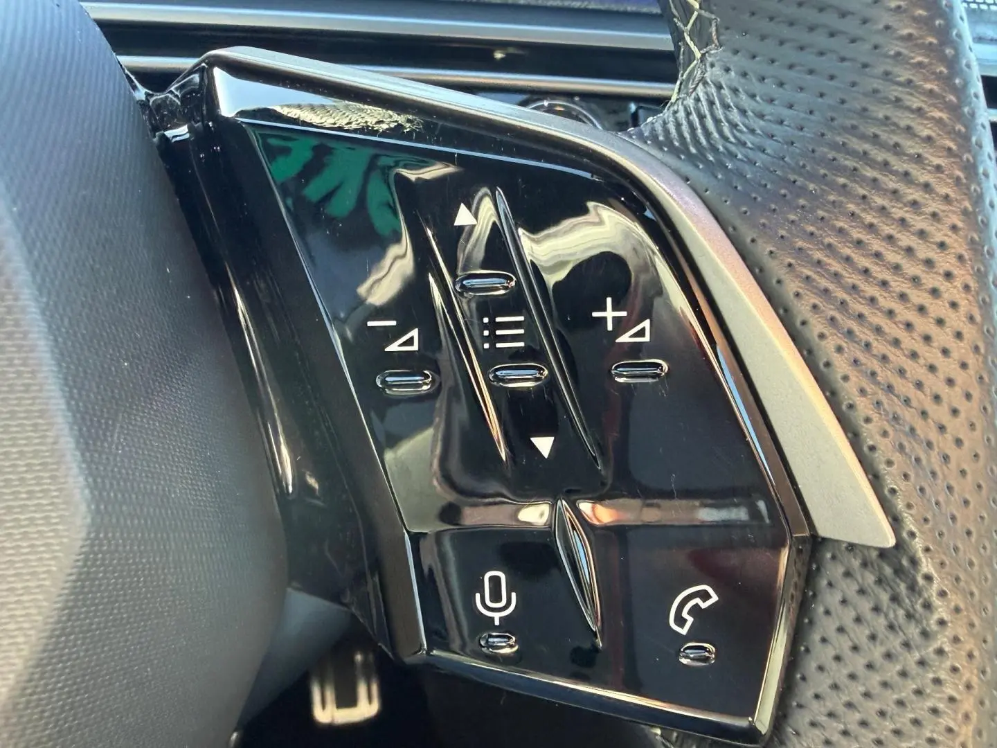 Gros plan sur les commandes noires du volant cuir perforé du Peugeot 5008 Hybrid blanc Okénite.