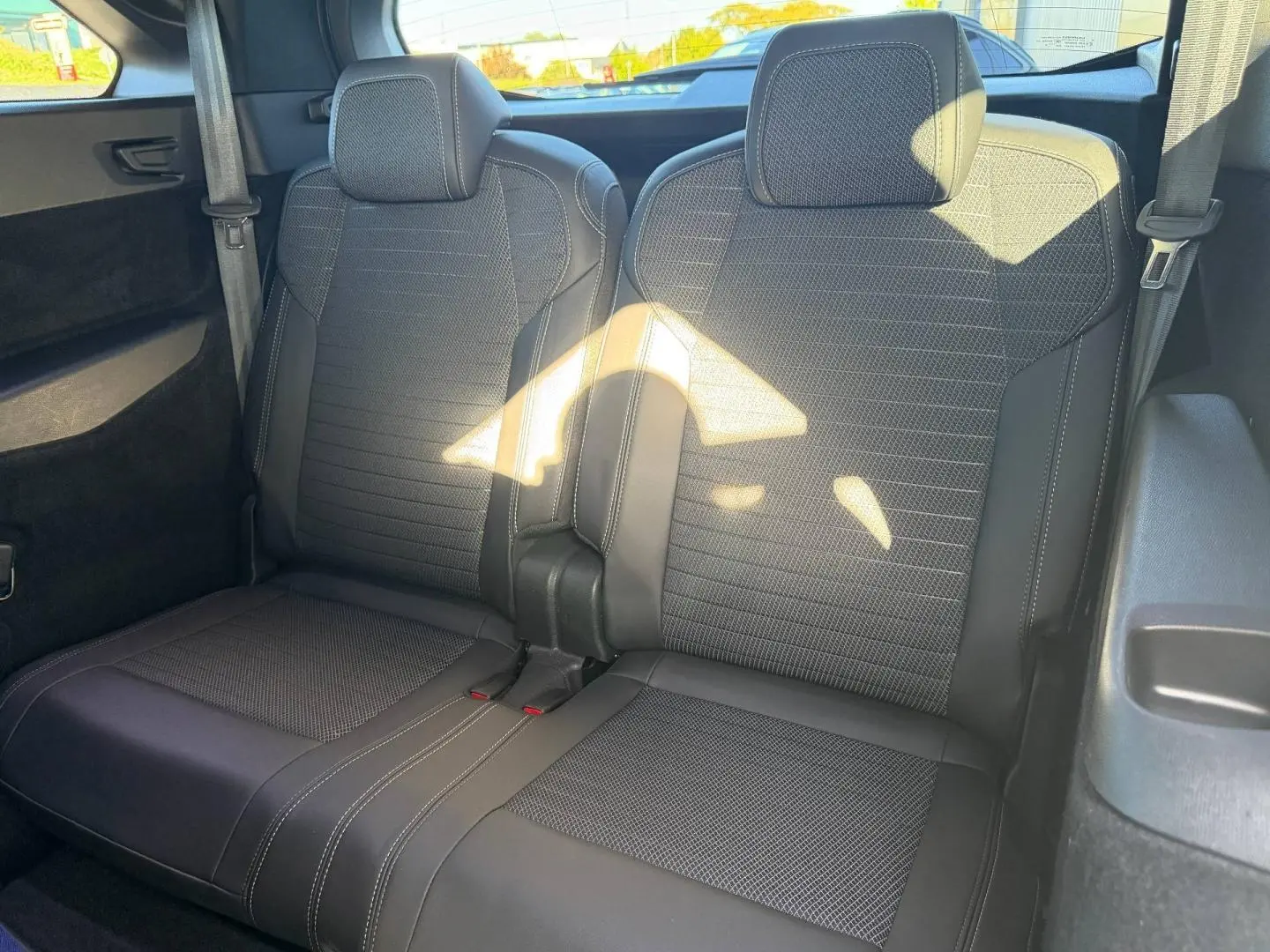 Vue rapprochée des deux sièges arrière noirs en tissu et cuir du Peugeot 5008 Hybrid 2025, avec ceintures visibles.