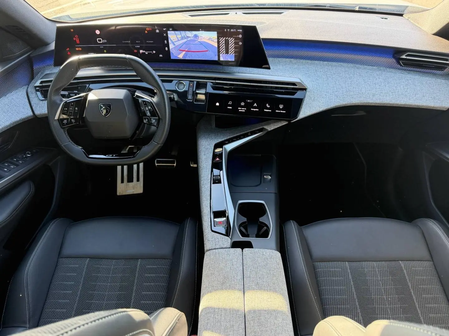 Vue intérieure avant du Peugeot 5008 Hybrid GT 2025, tableau de bord gris clair avec volant cuir noir multifonction et écran tactile large.