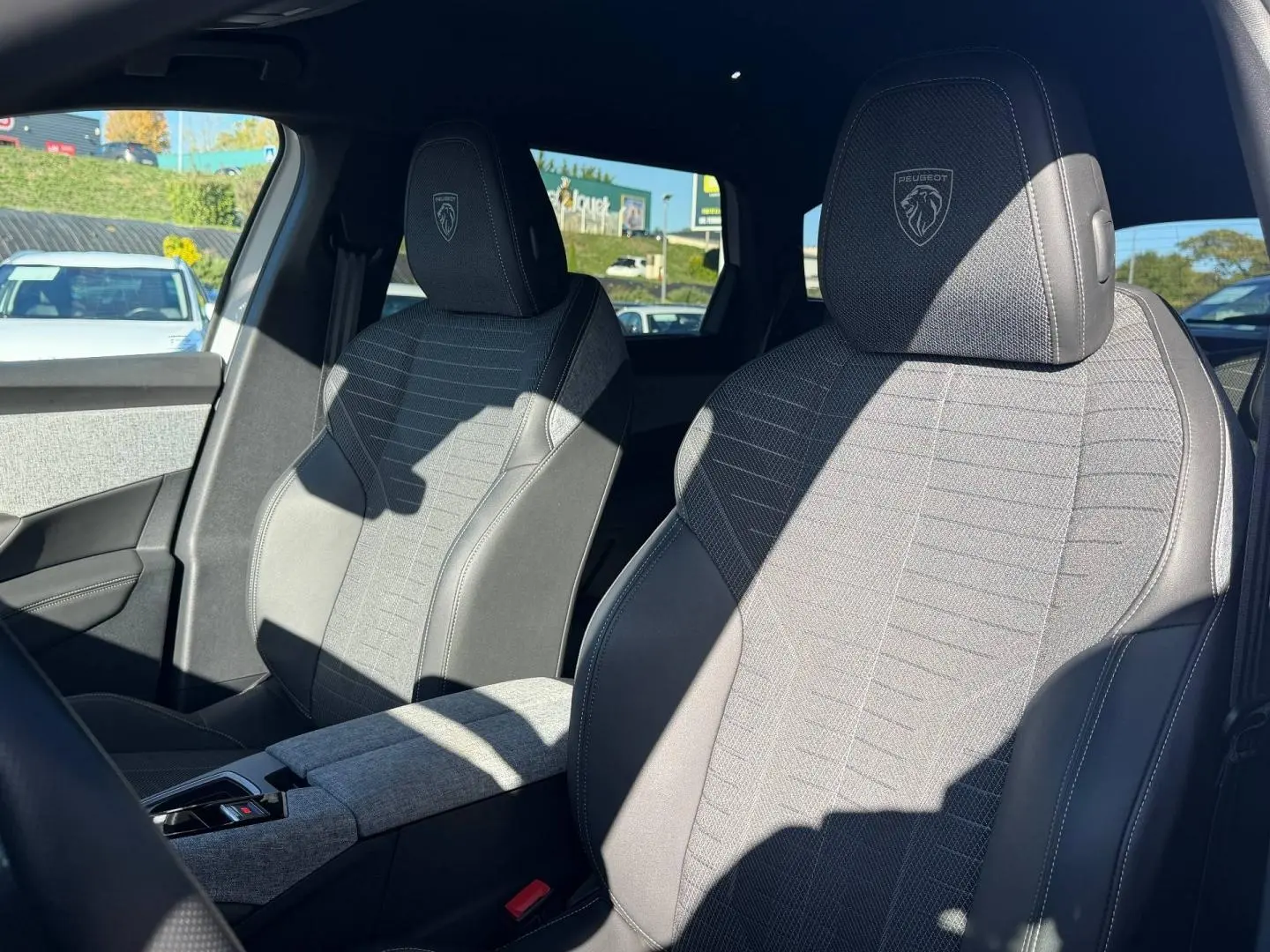 Vue intérieure sur les sièges avant gris tissu et cuir du Peugeot 5008 Hybrid 145ch GT, avec logo Peugeot brodé.
