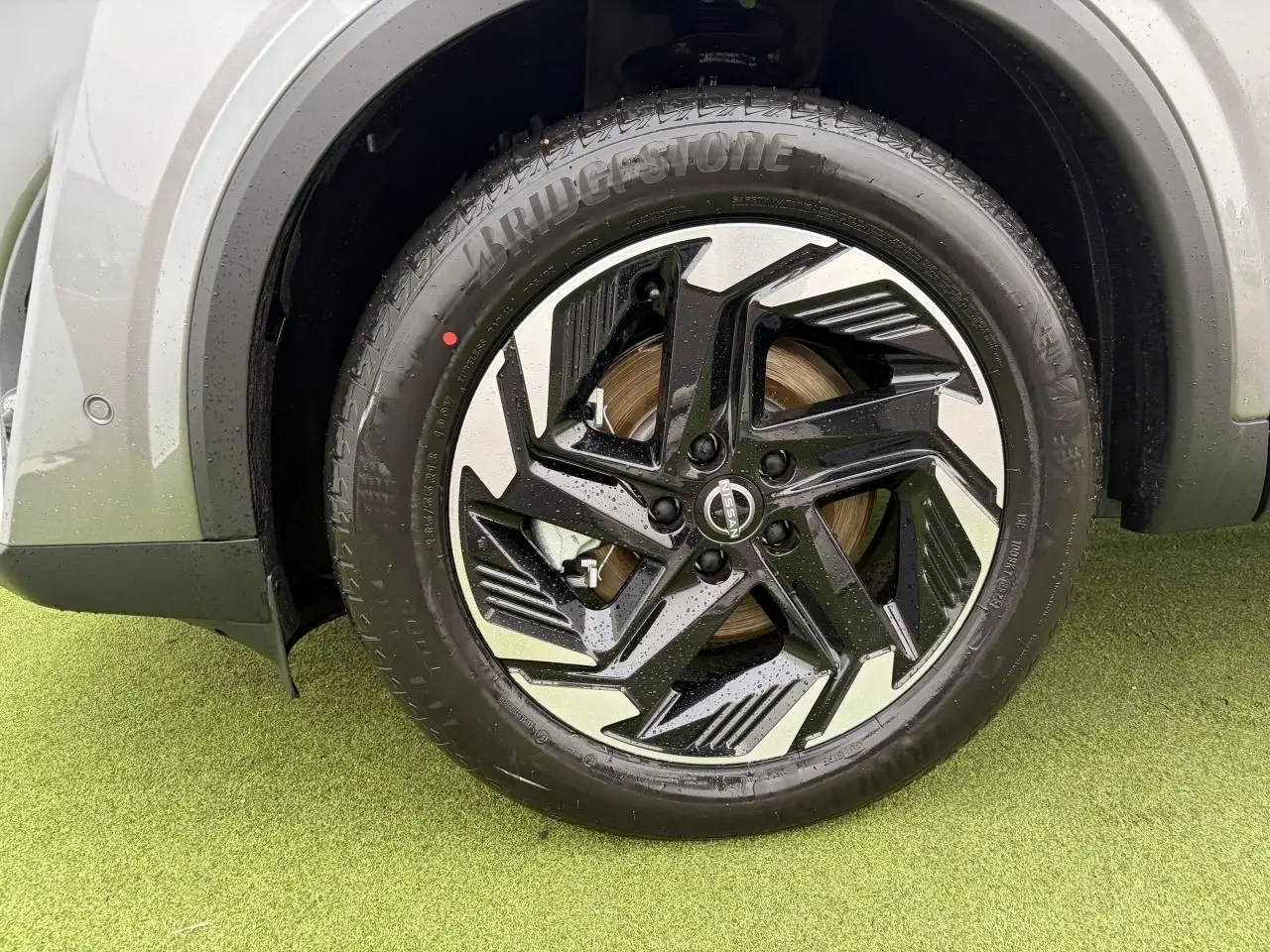 Gros plan sur la roue avant gauche du Nissan Qashqai III 2025, jante alliage 18" noire et argentée, carrosserie gris foncé.