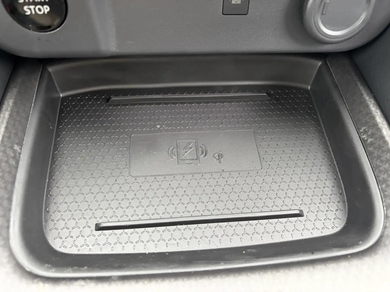 Gros plan sur le chargeur à induction noir dans la console centrale du Nissan Qashqai III gris foncé hybride 2025.
