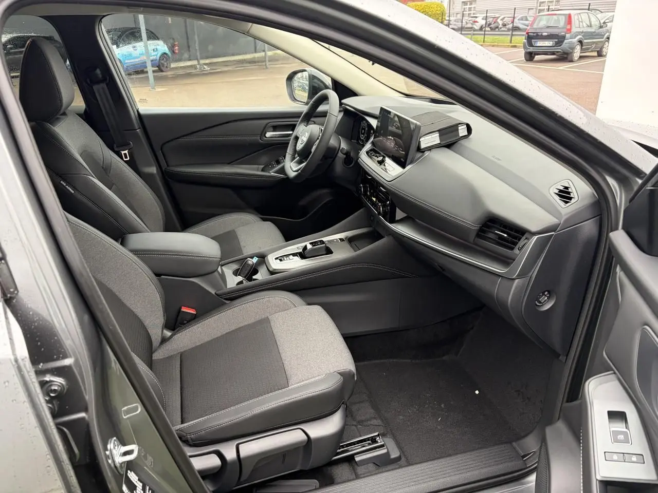 Intérieur côté conducteur du Nissan Qashqai 2025 gris foncé, avec sièges bi-matière, tableau de bord moderne et écran tactile.