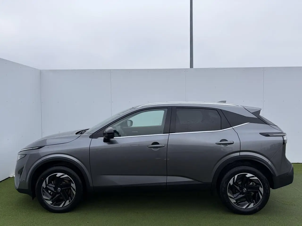 Profil côté gauche du Nissan Qashqai III 2025 en gris foncé métallisé avec jantes alliage noires et vitres teintées.