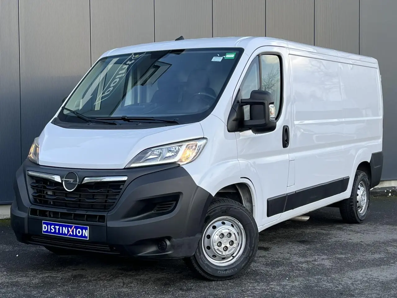 Fourgon Opel Movano blanc vu en 3/4 avant droit, avec calandre noire et rétroviseurs noirs rabattables.