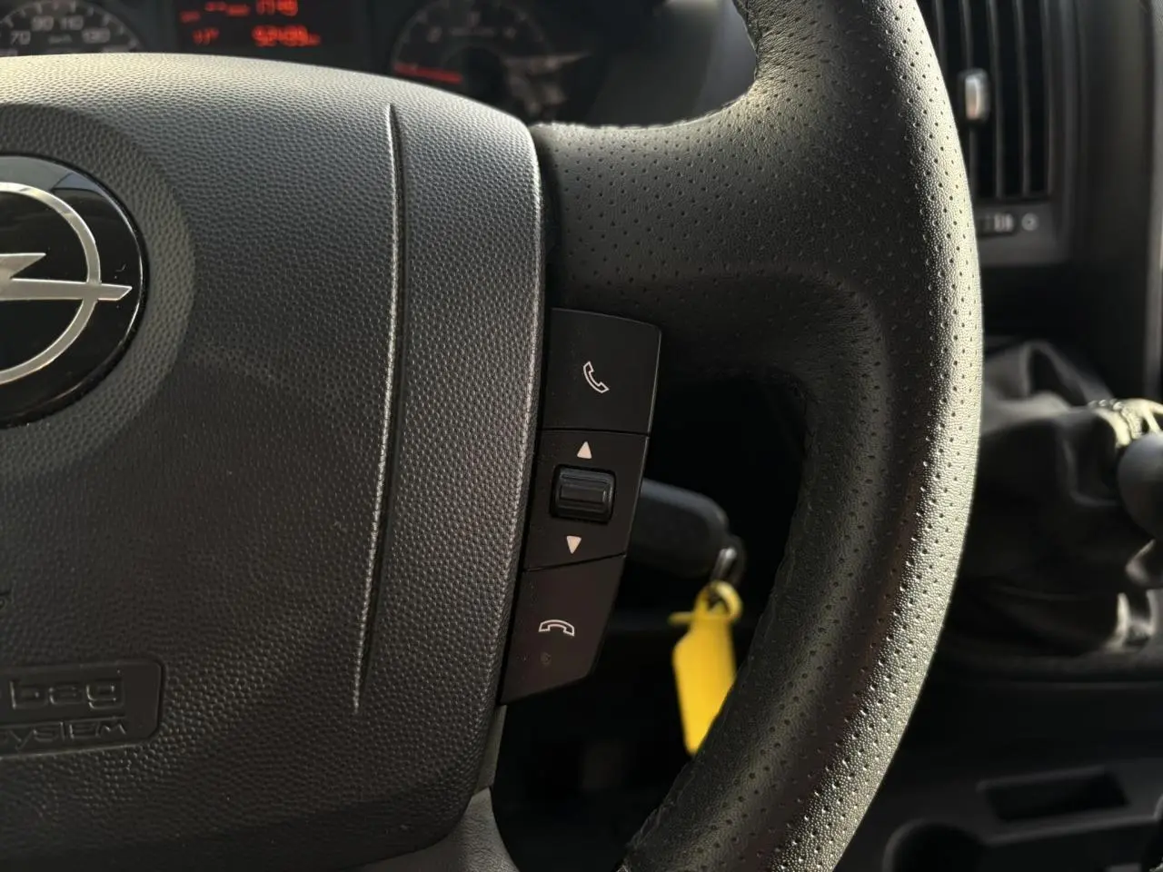 Gros plan sur le volant noir perforé d’un Opel Movano 2024 avec commandes d’appel et levier de vitesses manuel visible.