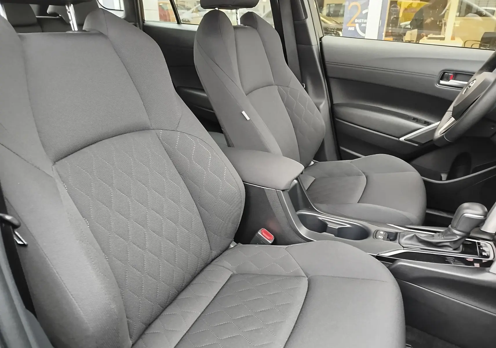 Vue intérieure côté droit du Toyota Corolla Cross 1.8 140ch Dynamic 2025, sièges tissu gris avec console centrale et levier de vitesse.