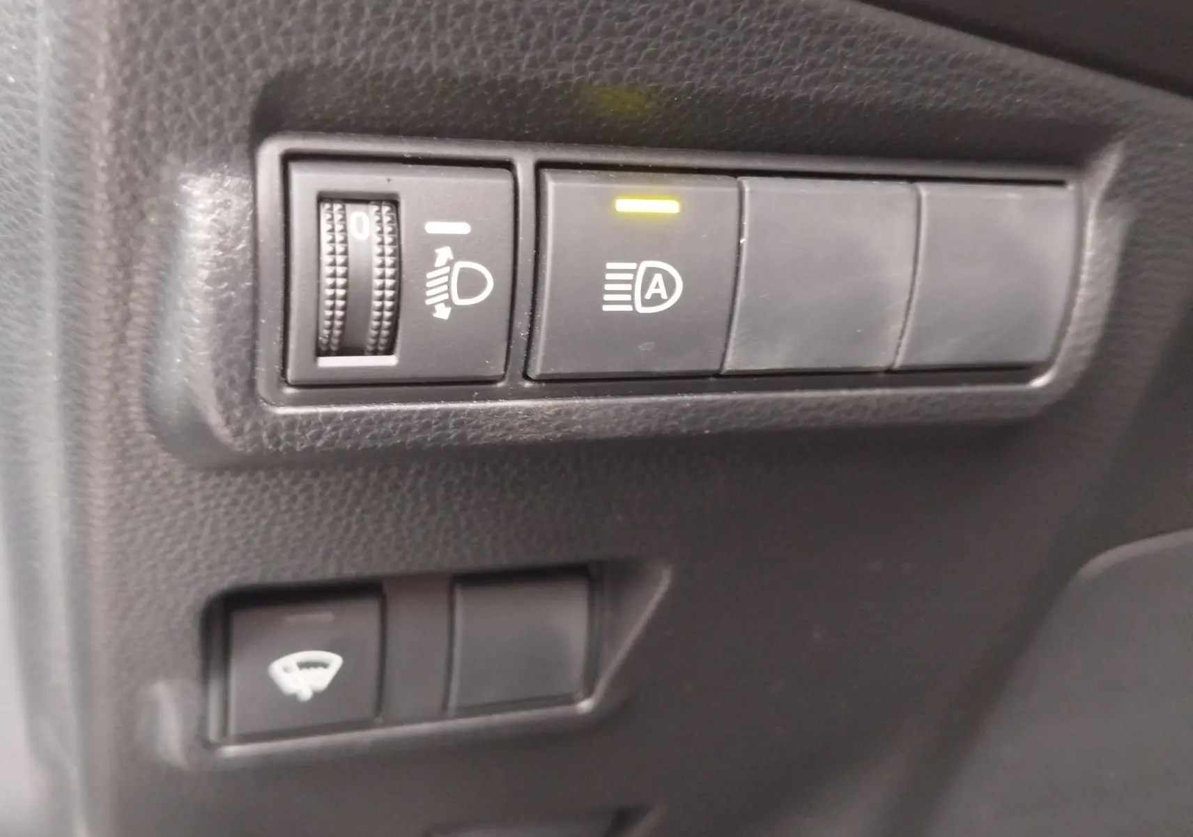 Détail des commandes intérieures noires du Toyota Corolla Cross 1.8 140ch Dynamic, avec réglage des phares et activation automatique.