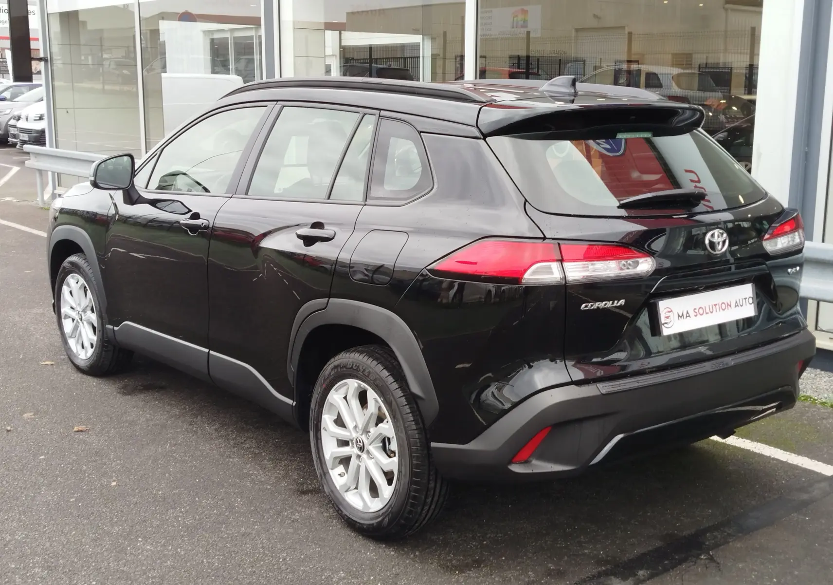 Vue 3/4 arrière droite d’un Toyota Corolla Cross noir intense avec jantes argent et feux arrière LED visibles.