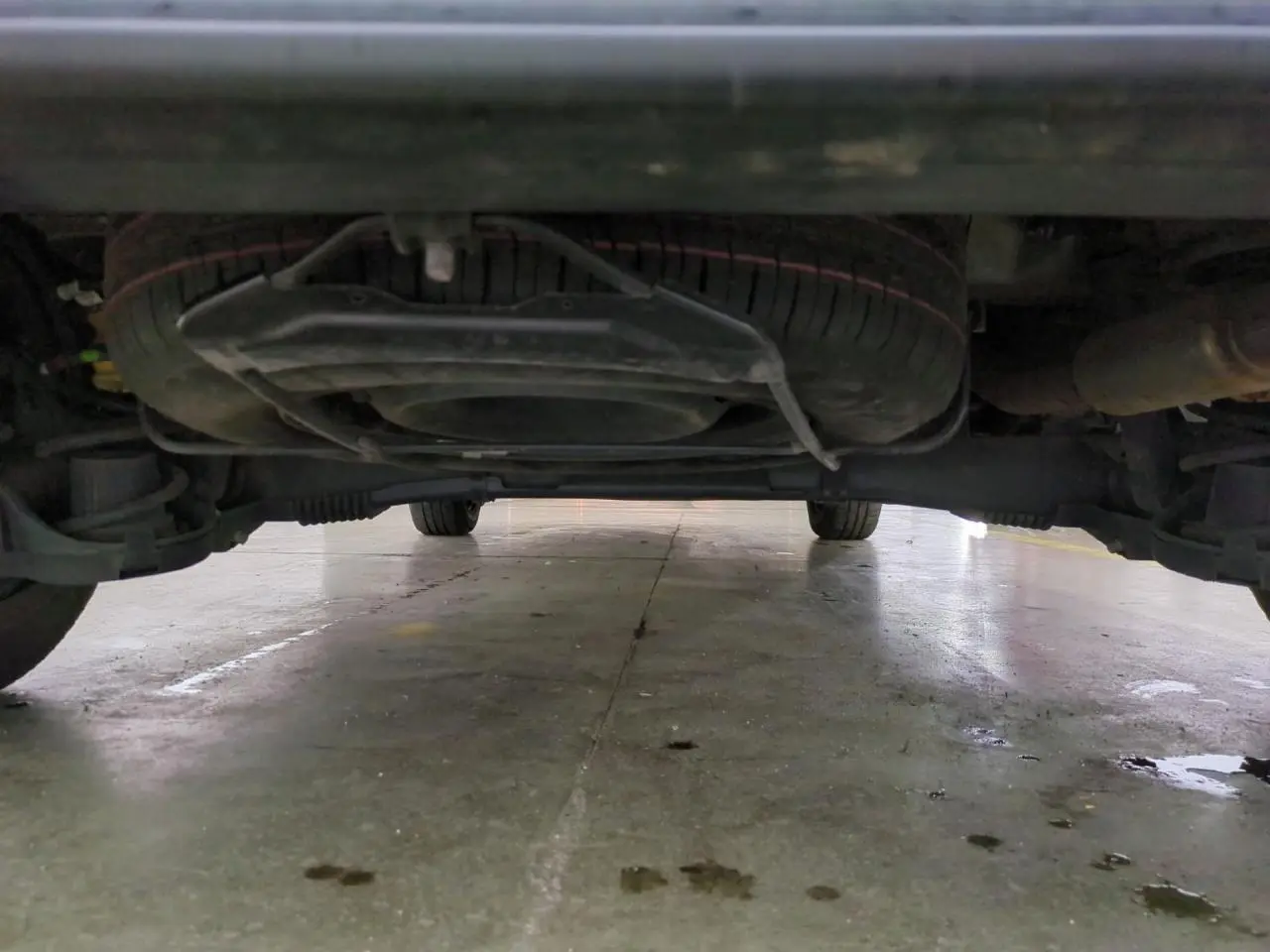 Vue en contre-plongée sous un Citroën Berlingo gris clair, montrant la roue de secours et le châssis.