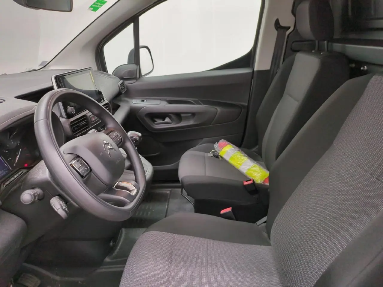 Vue intérieure côté conducteur du Citroën Berlingo gris clair, montrant le volant, la tablette tactile et les sièges tissu noirs.