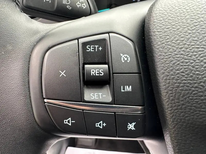 Gros plan sur les commandes noires du volant cuir multifonction du Ford Kuga 2024, avec boutons de régulateur et volume.