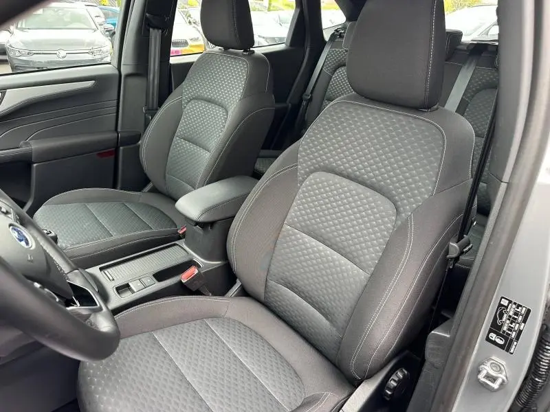 Vue intérieure côté conducteur du Ford Kuga 2024 gris Solar, sièges avant sport en tissu noir matelassé avec accoudoir central.