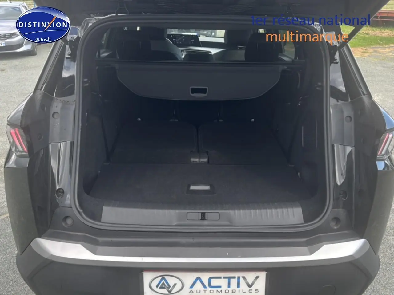 Coffre ouvert vu de l'arrière d'un Peugeot 5008 Hybrid 145 allure noir avec banquette rabattue et cache-bagages.