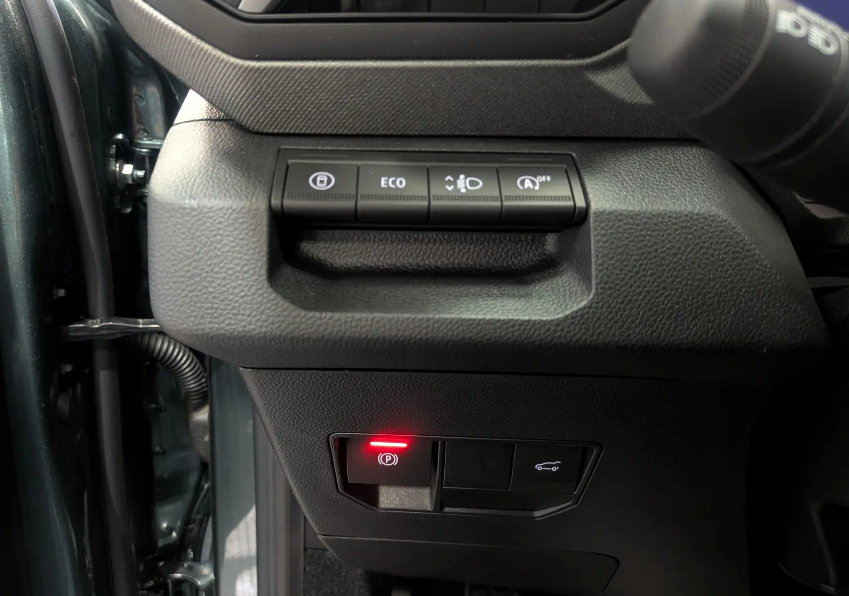 Vue rapprochée des commandes sur le tableau de bord côté gauche du Dacia Bigster Vert Cèdre, avec bouton de frein à main électronique allumé.